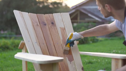 Diy man painting and applying protective varnish paint on a wooden garden chair
