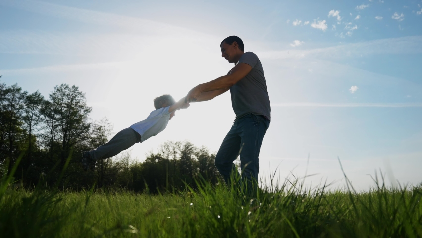 People in the park. happy family a playing in the park in summer. dad keeps whirling son and hands have. happy family kid dream concept. fun dad and son silhouette whirling green park | Shutterstock HD Video #1077383048