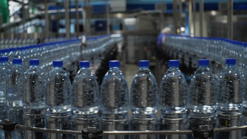 Bottles of clean drinking water are moving on a conveyor belt. Production of mineral water at a food processing plant | Shutterstock HD Video #1077383090