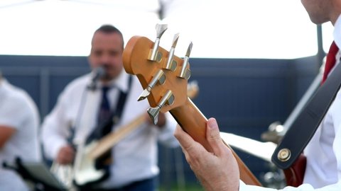 the band performs at a party in the foreground bass guitarist close-up hand with a guitar neck in the background other band members are out of focus