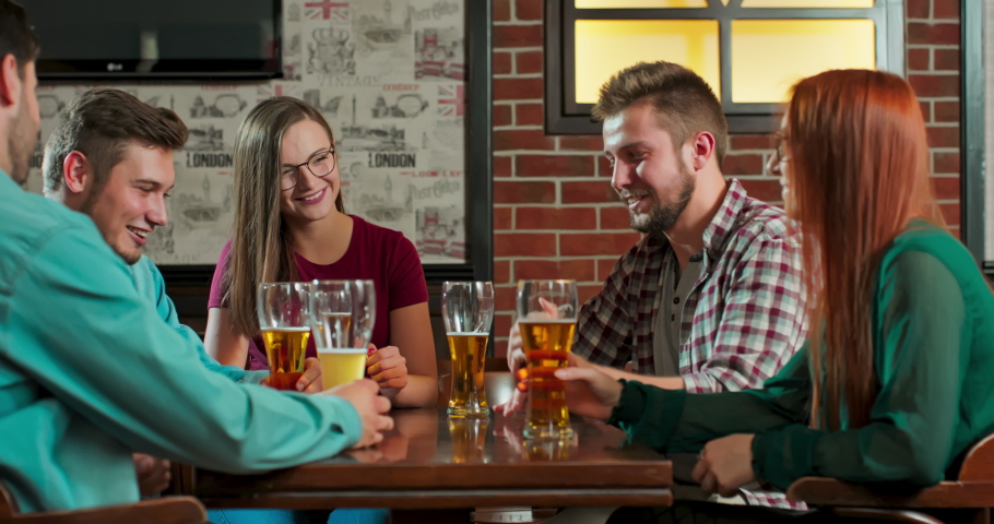 Friends do toasts, drink beer and cocktails while having a good time together at a bar