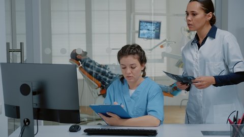 Professional team of dentist and nurse working on patient teethcare using dental x ray scan, stomatology equipment and computer at dentistry clinic. Orthodontists with medical tools
