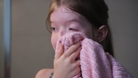 little girl wipes her face with a towel in the bathroom after washing her face