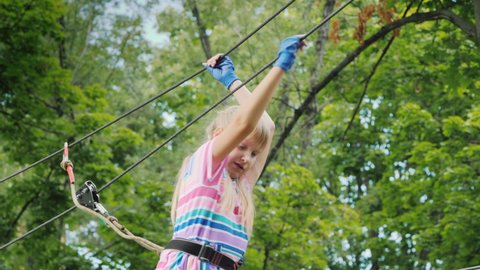 The child moves on ropes high in the crown of a tree. Entertainment at summer camp