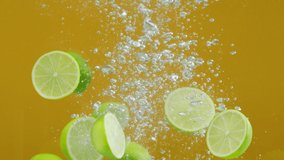 Close-up of falling ripe limes into the sparkling water on yellow background, making a cocktail of citrus fruits, drinking cold lemonade, shooting of carbonated water with floating sliced fruits.  - Powered by Shutterstock - Get 15% off with code: PIKWIZARD15