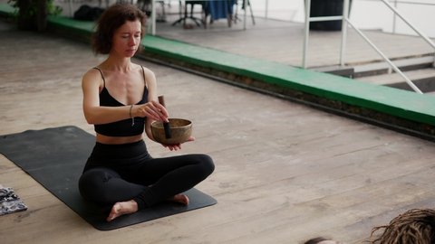 Woman holding singing bowls in her hands lead yoga class outdoors