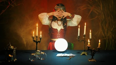 Night before Christmas, pagan girl fortune telling. Fantasy woman witch forecaster in old vintage costume predicts fate on magical glass ball. Backdrop streaming mystical fog, dark gothic room