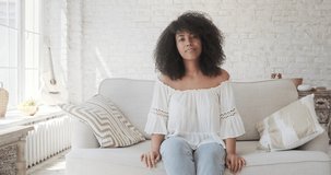 Happy black mixed woman looking at web camera waving hand and greeting. Online conversation by videocall. Vlogger starting livestream, recording video for social media at boho style apartment.