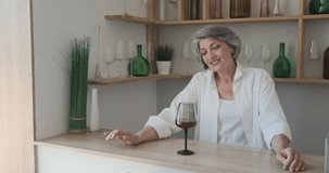 An older senior woman dances in the kitchen while drinking wine and feeling free of senior years. Enjoying the music and movement.