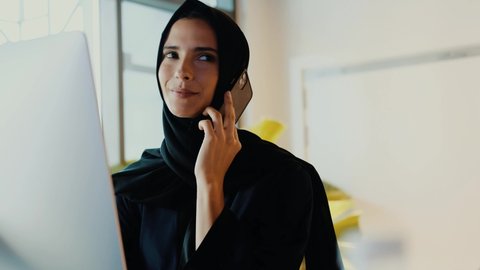 Working from home or office of Arab woman in Hijab Abaya. Beautiful Emirati national using smartphone talking concept. Female Arabic on call using mobile cell phone. 4K raw footage