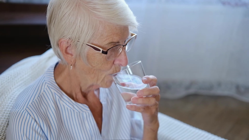 portrait caucasian healthy senior adult woman holding glass drinking fresh mineral pure water at home. maintaining health in old age concept. Royalty-Free Stock Footage #1077407513
