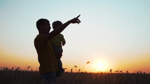 Farmer with his son in wheat field at sunset. Happy family. Father farmer holds his son in arms in wheat field. Family reaches out to sun. Farmer at sunset holds his son in arms. Happy family concept