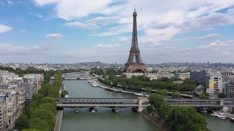 France, Paris Tour Eiffel (Eiffel Tower), cloudy summer day, with Pont d'Iena and Bir-Hakeim Bridge. Long drone shot, aerial view along the Seine river.