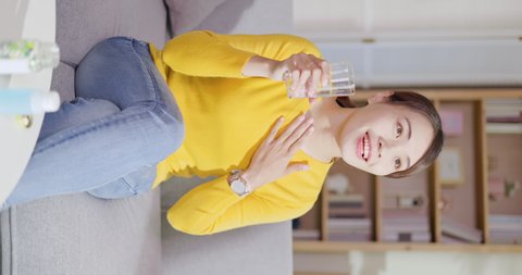 vertical close up of asian woman takes medicine or vitamin by water in living room at home