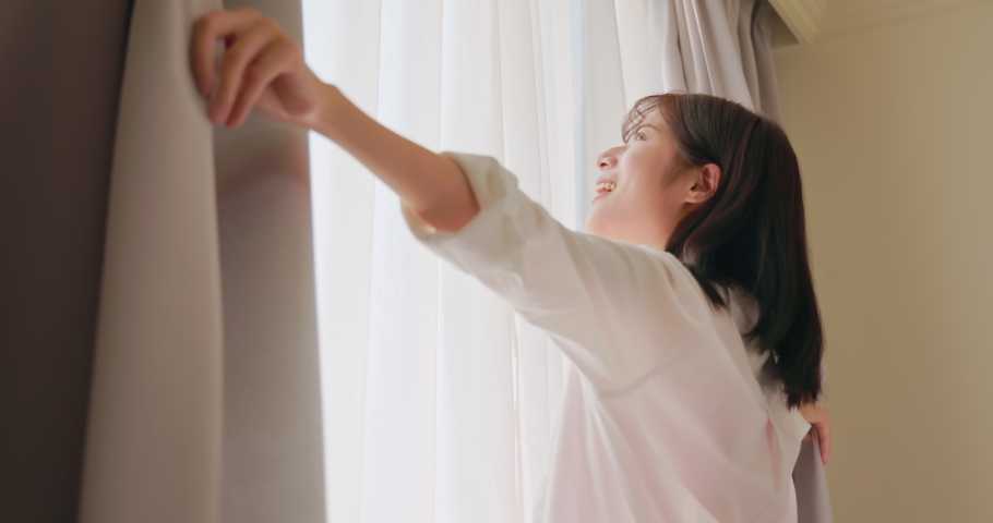 Close up of smiling asian woman turning around after opening curtain at home in slow motion | Shutterstock HD Video #1077413999
