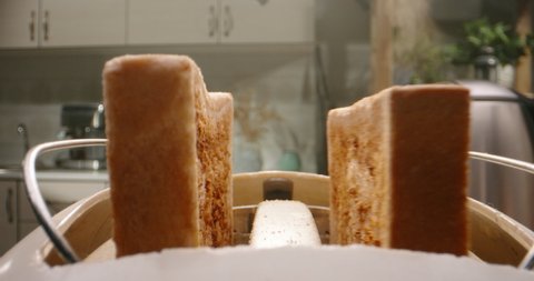 Close up shot of white sliced bread popping out of toaster with water steaming out of kettle on background - breakfast preparation 4k footage