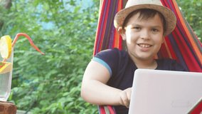 boy in a hammock uses a laptop. Communicates online on vacation. resting in a hammock, drinking a cocktail. Works online. Leads the stream. Plays a video game. Blogger