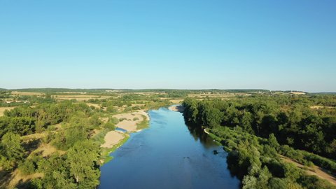 The river called Loire on the outskirts of Imphy and Nevers surrounded by wheat fields and green forests in Nièvre, Burgundy, France, in summer and by drone on a sunny day.