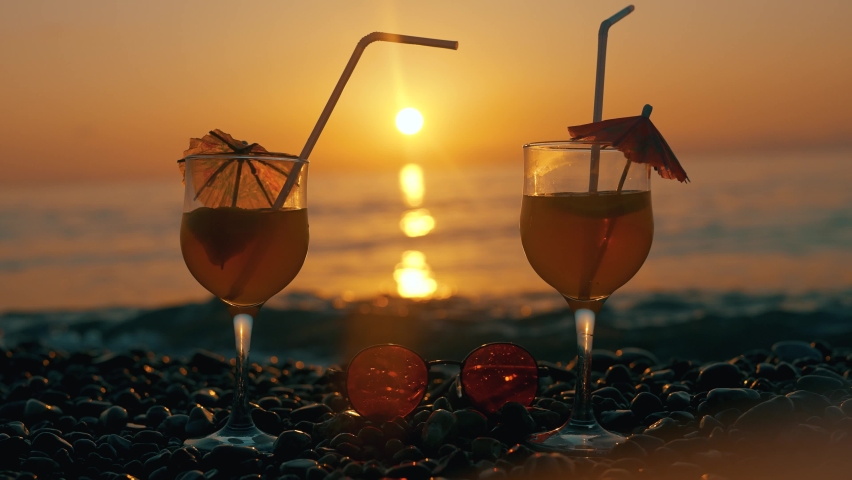 A romantic couple are clinking with glasses and enjoying summer sunset on background of a sea. Lovers are drinking cocktails. Concept of honeymoon or romantic travel or relax and holidays. Close up. Royalty-Free Stock Footage #1077434474