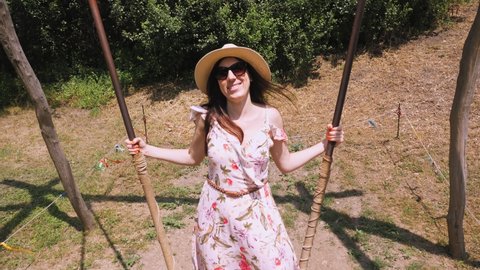 swinging. Happy young woman, in sunglasses and hat, having fun swinging on a big wooden swing, in the park, sunny summer day. Happy mood