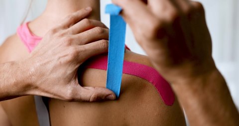 kinesiotaping - physiotherapist taping injured patient shoulder with kinesio tape after muscle injury. kinesiology