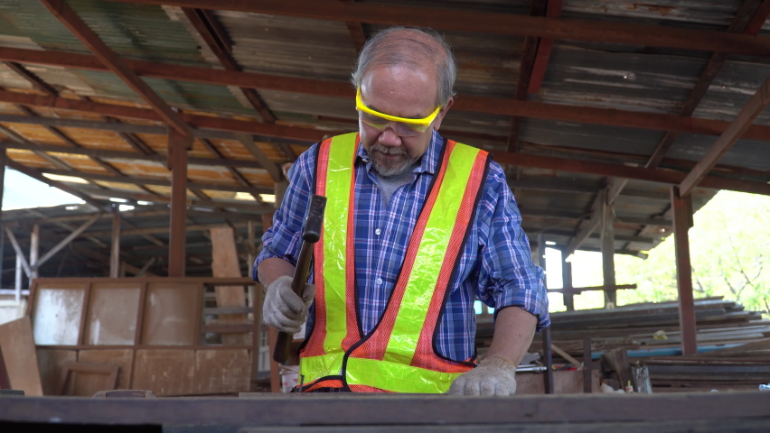 old asian carpenter hammer a nail on wood  in workshop . senior craftsman working
