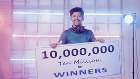 Excited Professional esports gamer with headphones celebrating and dancing by holding winners price money presentation at video gaming tournament on stage for victory