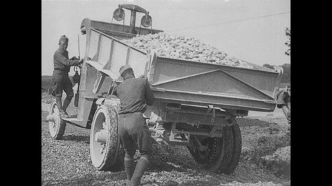 1920s: Men dump rocks off dump truck. Laborers shovel rocks off railcar. Man drives horses pulling wagon.