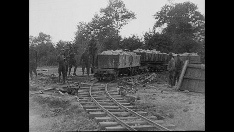 1920s: Railcars containing rock move along track. Laborers shovel rocks and sand from railcar.