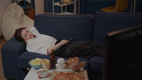 Businesswoman falling asleep on couch after eating meal from takeaway fast food place in living room. Sleepy person laying on sofa after work watching television while having food on table