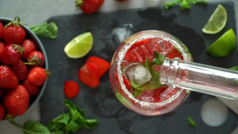 Top view of hands put ice in glass, pour berry soda and stir cocktail. Bartender prepares Mojito cocktail with lime and strawberry
