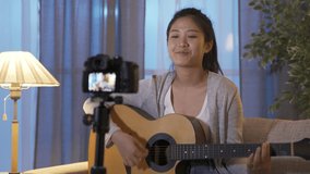 korean amateur singer sitting in front of camera is recording cover songs. singing and playing guitar. cheerful asian young lady is shooting footage and going to upload vocal music onto her channel.