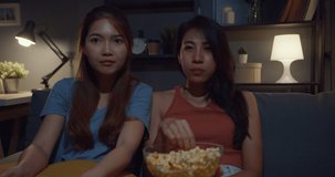 Attractive Asia couple ladies with casual enjoy happy moment focus watch online movie entertainment eat popcorn site on couch living room in home at night. Lifestyle activity quarantine concept.