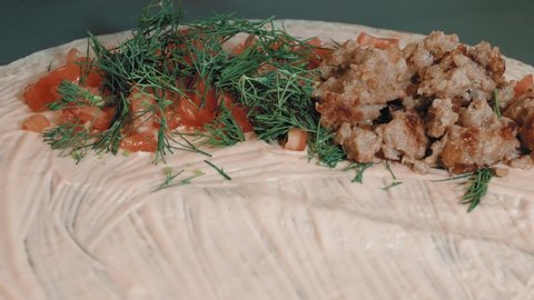 Delicious minced meat is laid out on a round pita bread. Fresh tomatoes and herbs are also added. Women's hands begin to twist the pita bread into a tube. A woman in the kitchen is preparing a snack.