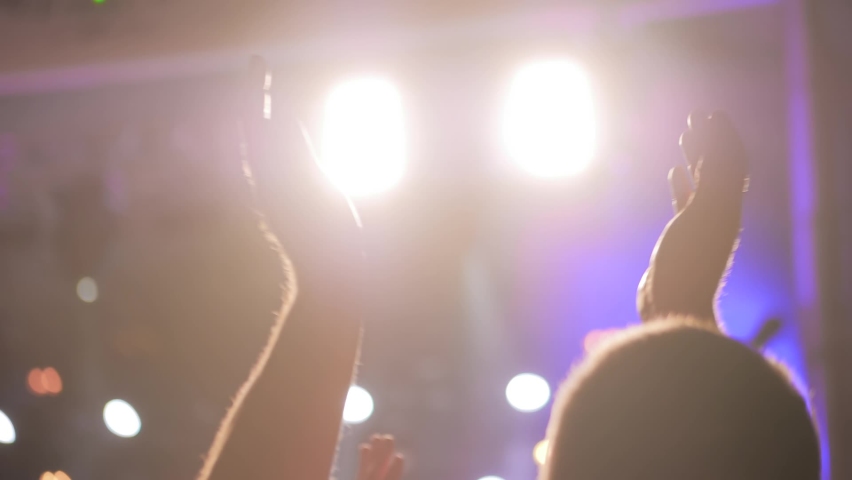 Slow motion: man partying, cheering, raising hands up and clapping at rock concert in front of stage of nightclub - close up. Bright colorful stage lighting. Nightlife and entertainment concept Royalty-Free Stock Footage #1077458831