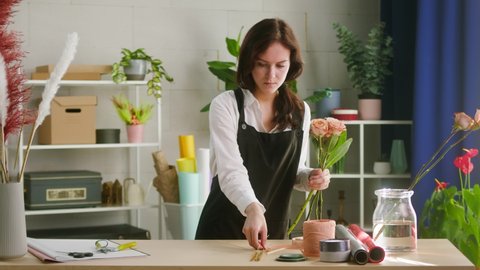 Young florist making bouquet of roses and dried flowers at workplace. Floral artist working in flower shop studio. Floristry showing masterclass on creating flower arrangement. Small woman business.