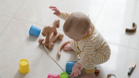 Little baby walks barefoot on the floor with toys scattered around at home. Child playing Making first steps.