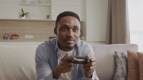 Upset african american gamer playing console games and loosing a round indoors