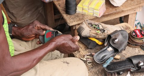 NIMA, GHANA - 20 JUL 2021: Old Man Shoe maker outdoors cobbler shop Accra Ghana . Old Muslim shoe maker and cobbler. Poverty section of Accra Ghana. Happy to repair people shoes for very little income
