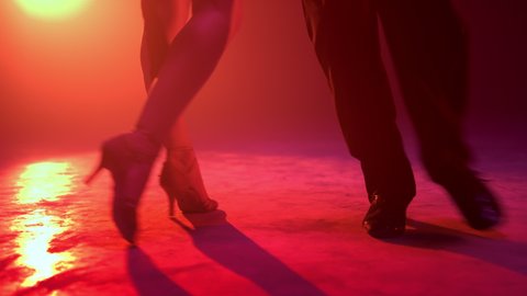 Closeup latin dancers legs practicing movement indoors. Unknown dance couple feet performing on illuminated stage. Unrecognizable passionate man and woman dancing in red lights background.