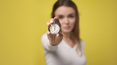 Stopwatch in foreground in hand of attractive young woman. stopwatch counts down from zero. Retro old vintage clock timer in hand of nice lady. little time left, clock is ticking. Yellow background