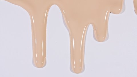 Foundation for face, smear, concealer, cosmetic liquid foundation, or cream beige color smudge flowing down on a white surface. Beauty skincare sample. Macro Shot