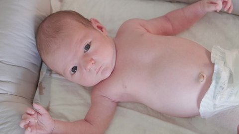 Newborn baby boy hiccups lying in bed, crib and child looks up suffering from hiccupping