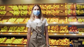 Portrait young woman worker seller in a Vegetable section supermarket standing in a protected face mask arms crossed. greengrocer female looking at camera in fruit shop market Employee in a work apron