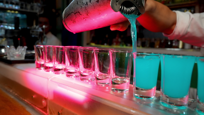 4K Professional male bartender pouring mixed blue liquor cocktail drink from cocktail shaker into shot glass on bar counter at nightclub. Mixologist barman making alcoholic drink serving to customer Royalty-Free Stock Footage #1077493529