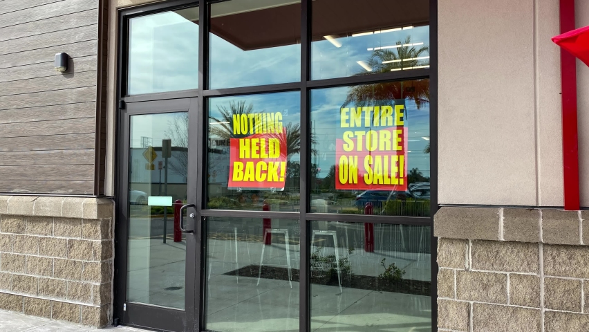 Zooming in on signs in the window of a retail store going out of business that say the entire store on sale, everything must go and nothing held back.
