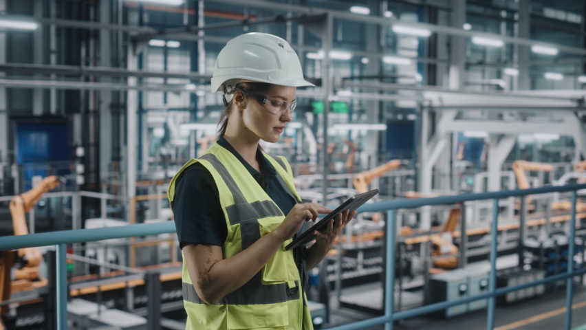 Female Car Factory Engineer in High Visibility Vest Using Laptop Computer. Automotive Industrial Manufacturing Facility Working on Vehicle Production with Robotic Arms. Automated Assembly Plant. | Shutterstock HD Video #1077496244