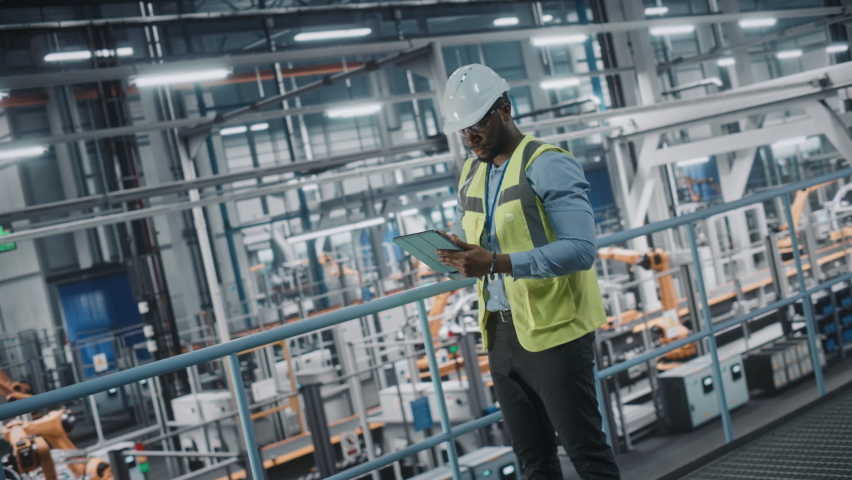 African American Car Factory Engineer in High Visibility Vest Using Tablet Computer. Automotive Industrial Manufacturing Facility Working on Vehicle Production on Automated Technology Assembly Plant. Royalty-Free Stock Footage #1077496277