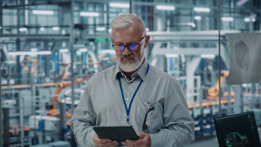 Car Factory Office: Portrait of Senior White Male Chief Engineer Using Tablet Computer in Automated Robot Arm Assembly Line Manufacturing High-Tech Electric Vehicles. Looking at Camera and Smiling Royalty-Free Stock Footage #1077501836