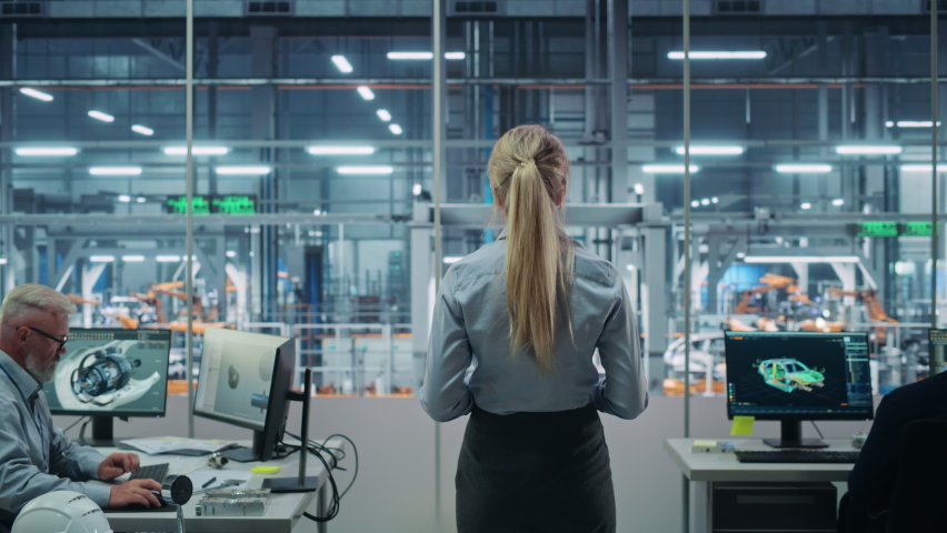 Car Factory Office: Successful Female Chief Engineer Overlooking Factory Production Conveyor. Automated Robot Arm Assembly Line Manufacturing Advanced High-Tech Electric Vehicles. Back View Shot | Shutterstock HD Video #1077501893